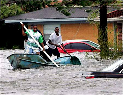 Three men use makeshift oars to paddle a damaged boat